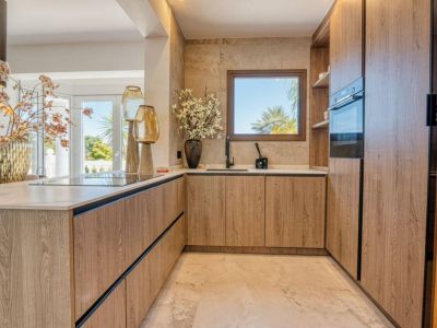 Detalle de la cocina con muebles de madera clara y encimera de mármol, iluminada con luz natural.