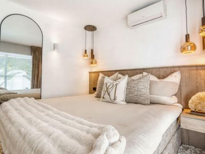Dormitorio con cabecero de madera, iluminación colgante dorada y espejo de cuerpo entero.