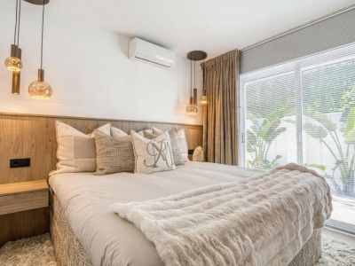 Dormitorio con cabecero de madera, lámparas colgantes de cristal y cortinas beige junto a la ventana.