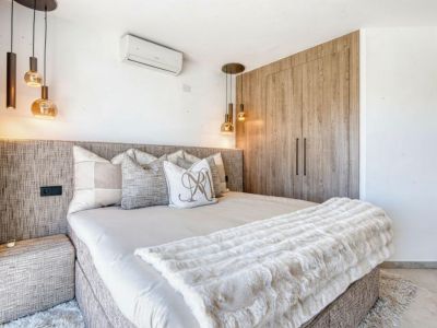 Dormitorio con cabecero tapizado, lámparas colgantes de diseño y armario empotrado de madera clara.