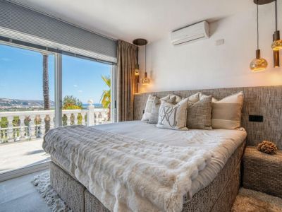 Dormitorio luminoso con acceso a terraza y vistas al mar. Cama con cabecero tapizado y ropa de cama en tonos neutros.