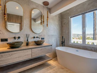 Elegante baño con lavabos de piedra sobre encimera de madera, bañera exenta y vistas panorámicas.