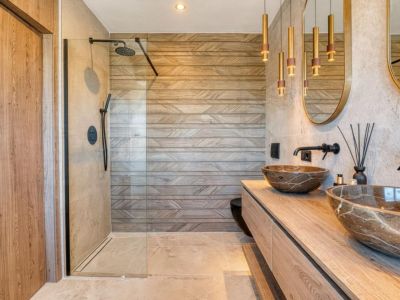 Elegante baño con lavabos de piedra y ducha con mampara de cristal, destacando el revestimiento de pared con diseño geométrico.
