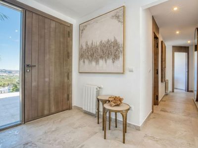 Entrada luminosa con puerta de madera y suelo de mármol. Detalle de obra de arte abstracta y mesas auxiliares.