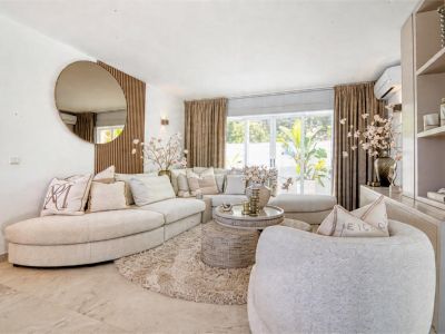 Luminoso salón con sofá modular beige, alfombra de felpa y espejo redondo decorativo.