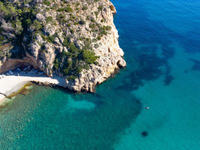 Vista aérea de una cala rocosa con botes en la playa y aguas turquesas.