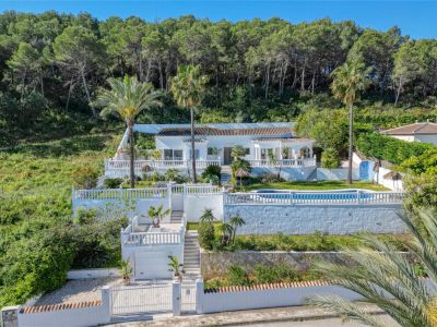 Vista exterior de la villa en Piver, Jávea, destacando su fachada blanca, piscina y jardines escalonados con vegetación mediterránea.
