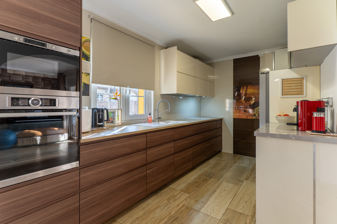 Cocina moderna con armarios de madera, encimera clara y suelo de baldosa imitación madera.