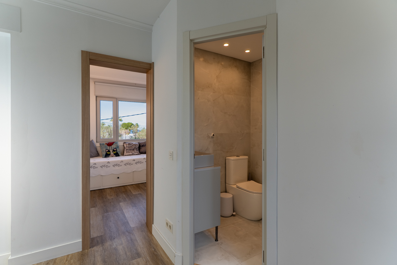 Detalle de pasillo con acceso a baño de mármol y dormitorio con luz natural.