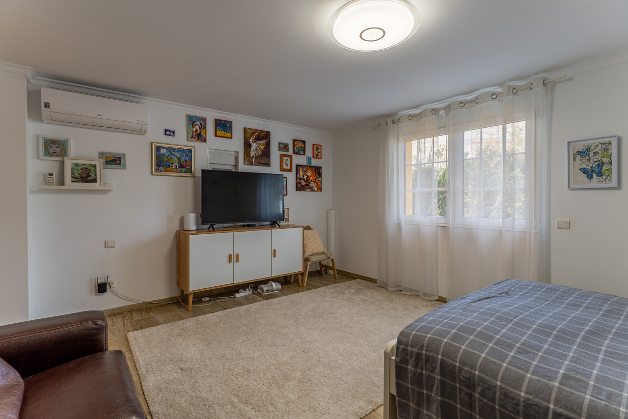 Dormitorio luminoso con alfombra de felpa, mueble de TV blanco y decoración artística en la pared.