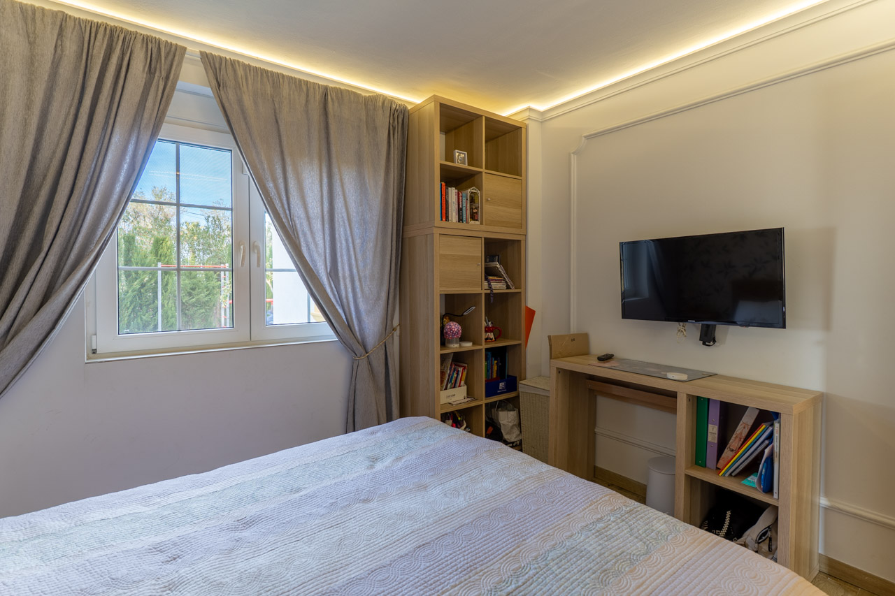 Dormitorio luminoso con estanterías de madera clara y cortinas grises junto a la ventana.