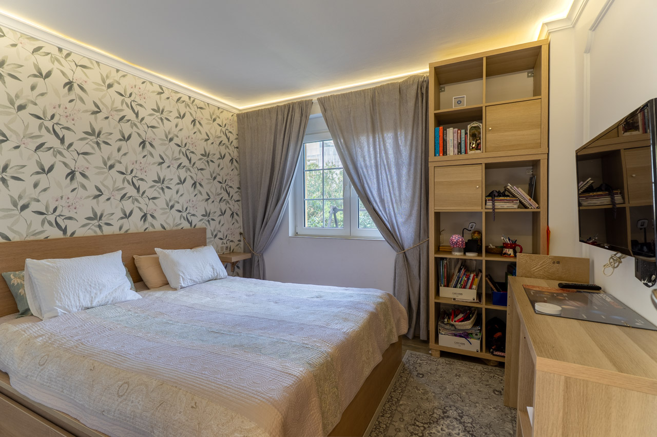 Dormitorio luminoso con papel pintado floral, cama de madera clara y estantería modular a juego.
