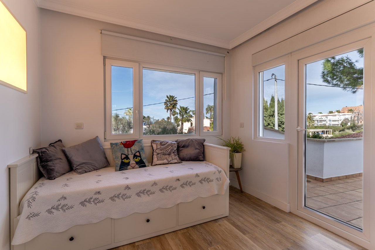 Dormitorio luminoso con sofá cama, vistas al exterior y acceso a terraza.