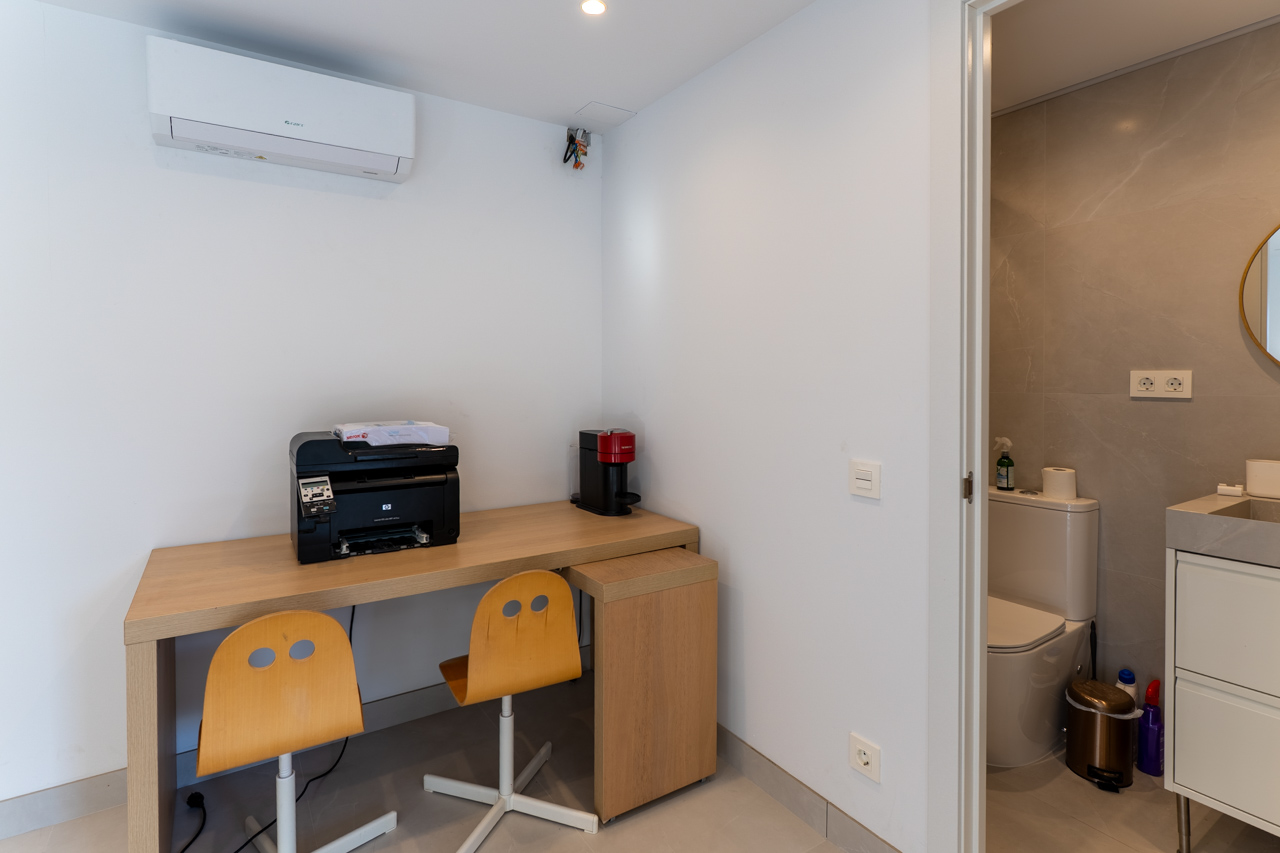 Rincón de trabajo funcional con escritorio de madera clara y acceso al baño en suite.