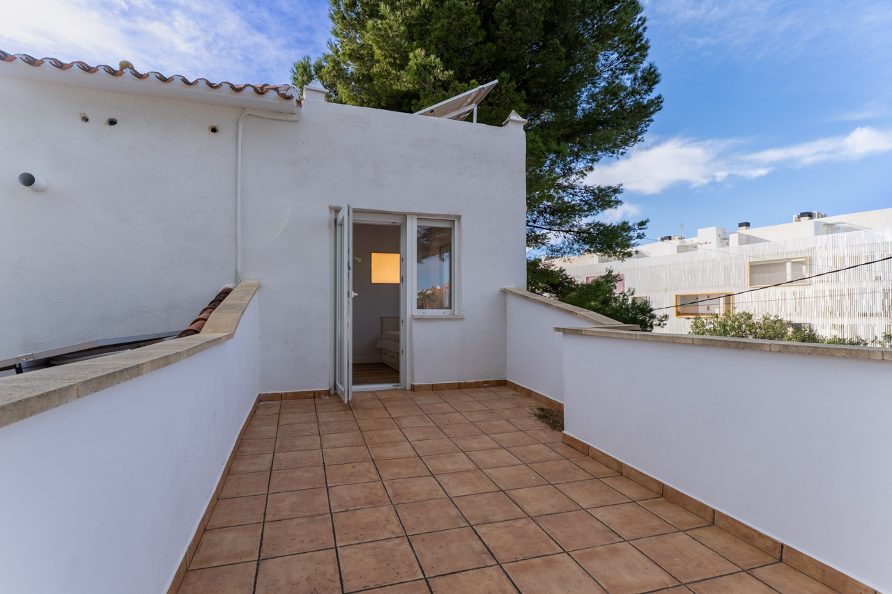 Terraza con suelo de baldosas y muros blancos. Puerta abierta a dormitorio luminoso.