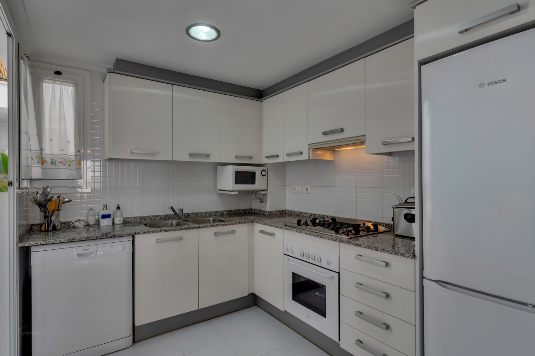 Cocina funcional con encimera de granito, electrodomésticos blancos y luz cenital.