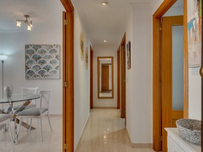 Detalle del pasillo con puertas de madera y suelo de baldosas color crema. Al fondo, espejo de cuerpo entero.
