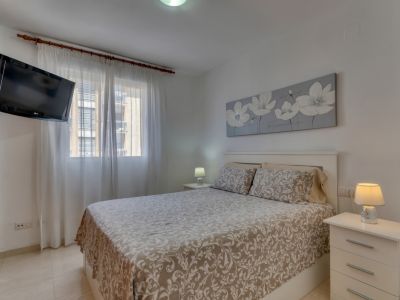Dormitorio luminoso con cama doble, mesitas de noche blancas y TV montada en la pared.