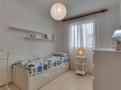 Habitación luminosa con cama individual, estantes decorativos y detalles náuticos.