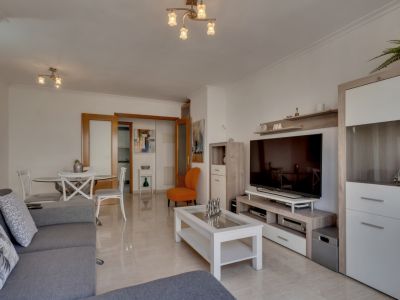 Salón luminoso con suelo de baldosas, sofá gris y mobiliario moderno en tonos neutros y blancos.