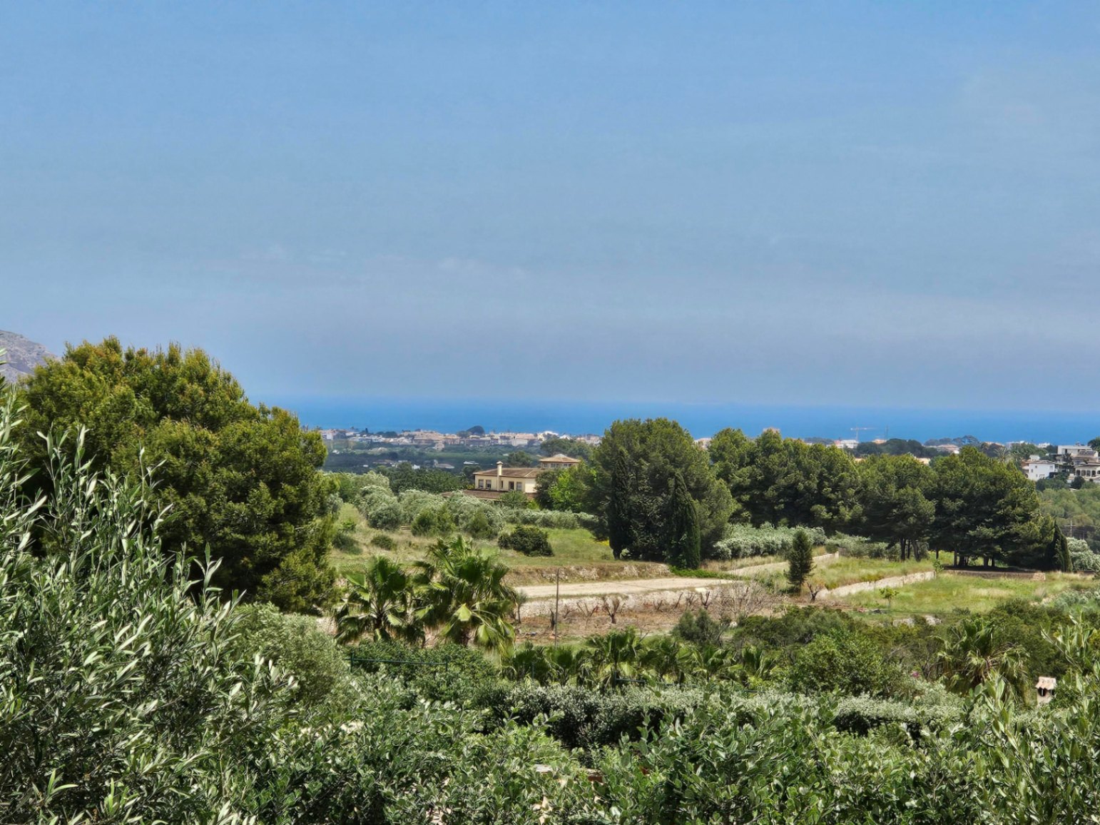 Vista panorámica de la villa rodeada de vegetación exuberante y el mar Mediterráneo al fondo.