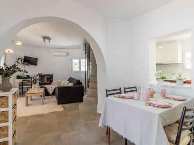Comedor luminoso con mesa preparada en tonos rosados y acceso al salón abovedado.