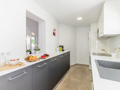 Detalle de la cocina con encimera blanca, armarios grises y suelo cerámico. Iluminación empotrada.