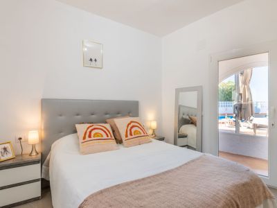 Dormitorio luminoso con cabecero gris, ropa de cama blanca y acceso directo a la piscina.
