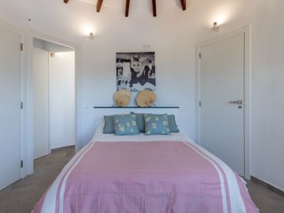 Dormitorio luminoso con cama doble, ropa de cama rosa y cabecero decorado con abanicos.