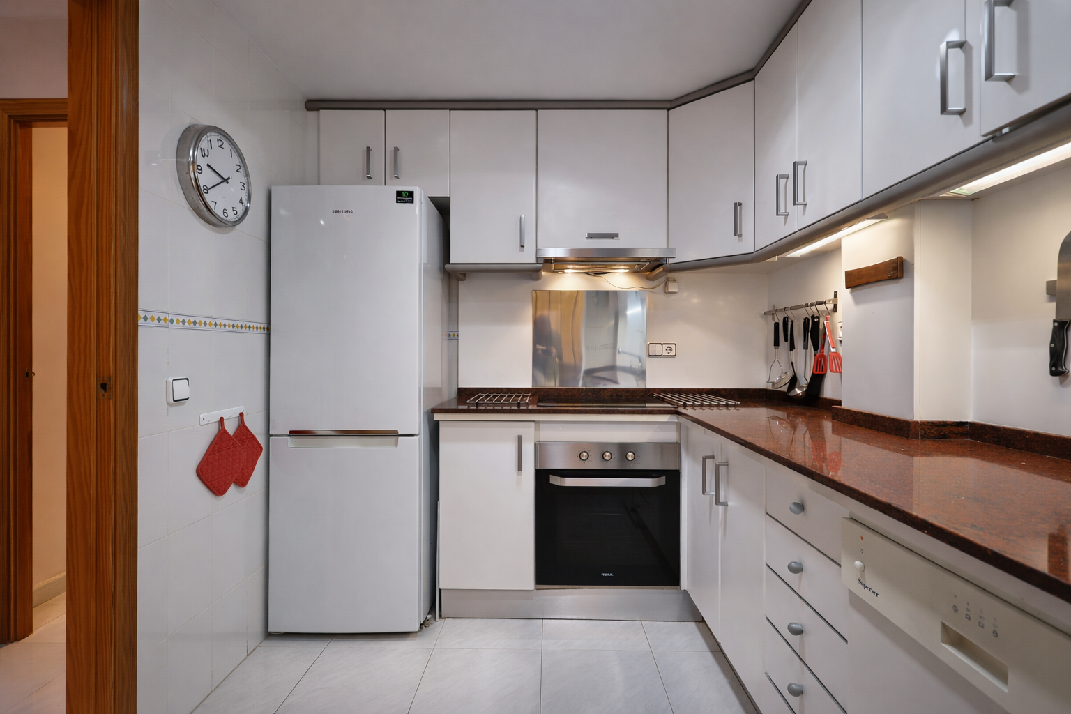Cocina funcional con encimera de granito, electrodomésticos blancos y armarios altos.