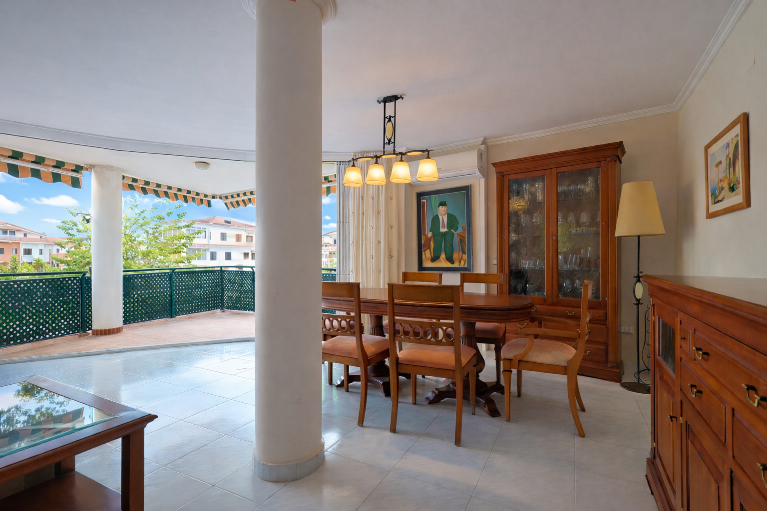 Comedor luminoso con acceso a terraza, destacando mobiliario clásico de madera y suelo de baldosas claras.