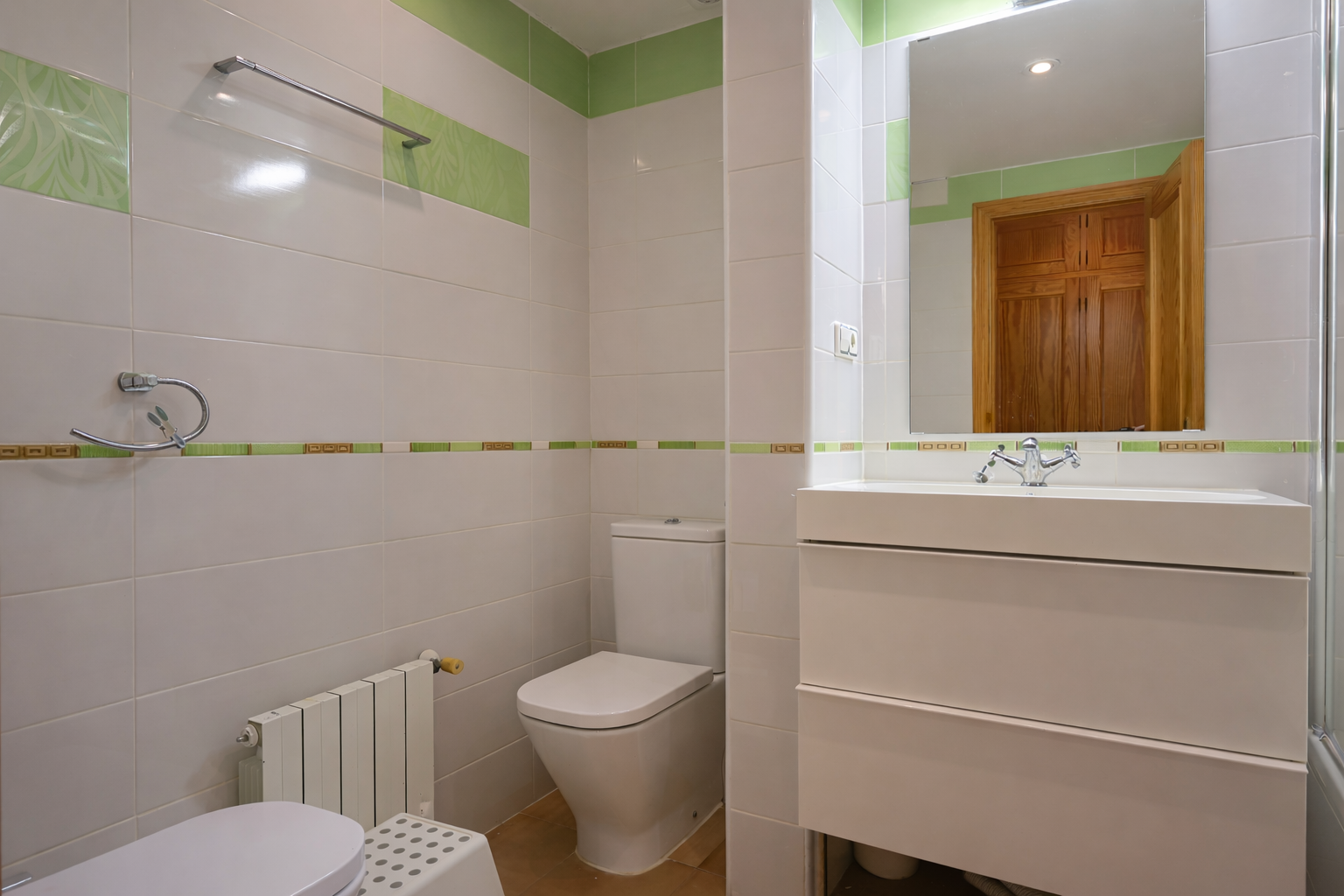 Cuarto de baño con azulejos blancos y detalles verdes, lavabo moderno y espejo.