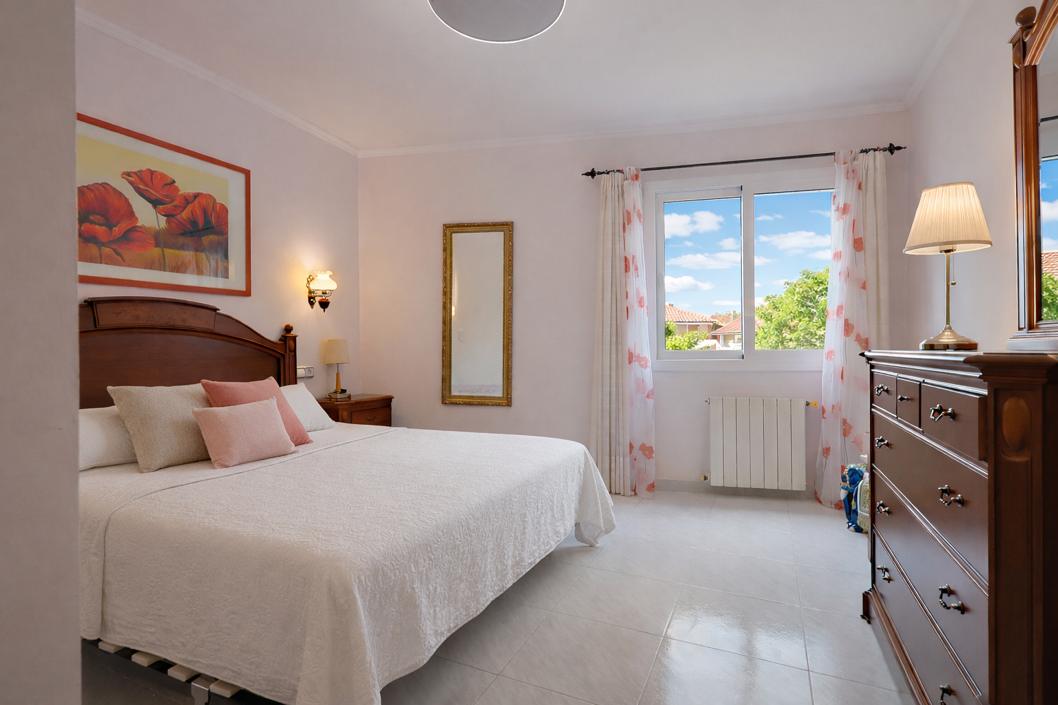 Dormitorio luminoso con cama de madera, cómoda clásica y vistas al exterior.