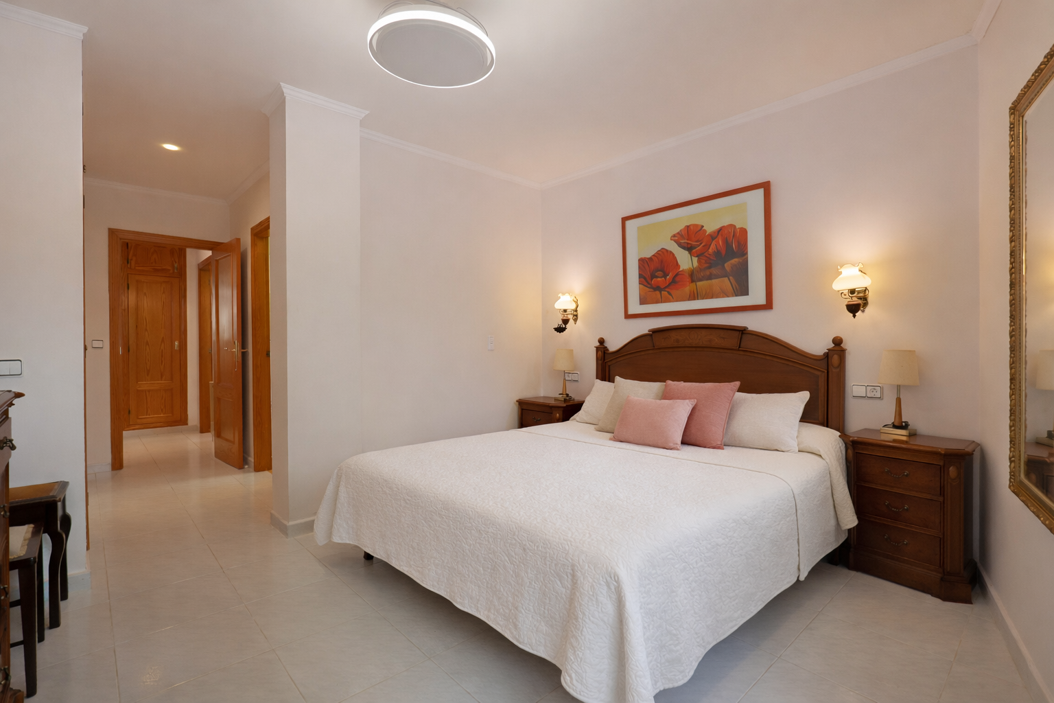 Dormitorio luminoso con cama doble, mesitas de noche de madera y suelo de baldosas.