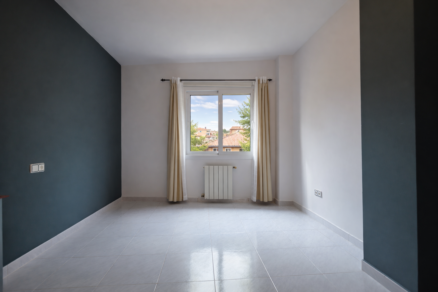 Habitación luminosa con pared en azul plomo, ventana con vistas y suelo de baldosas.