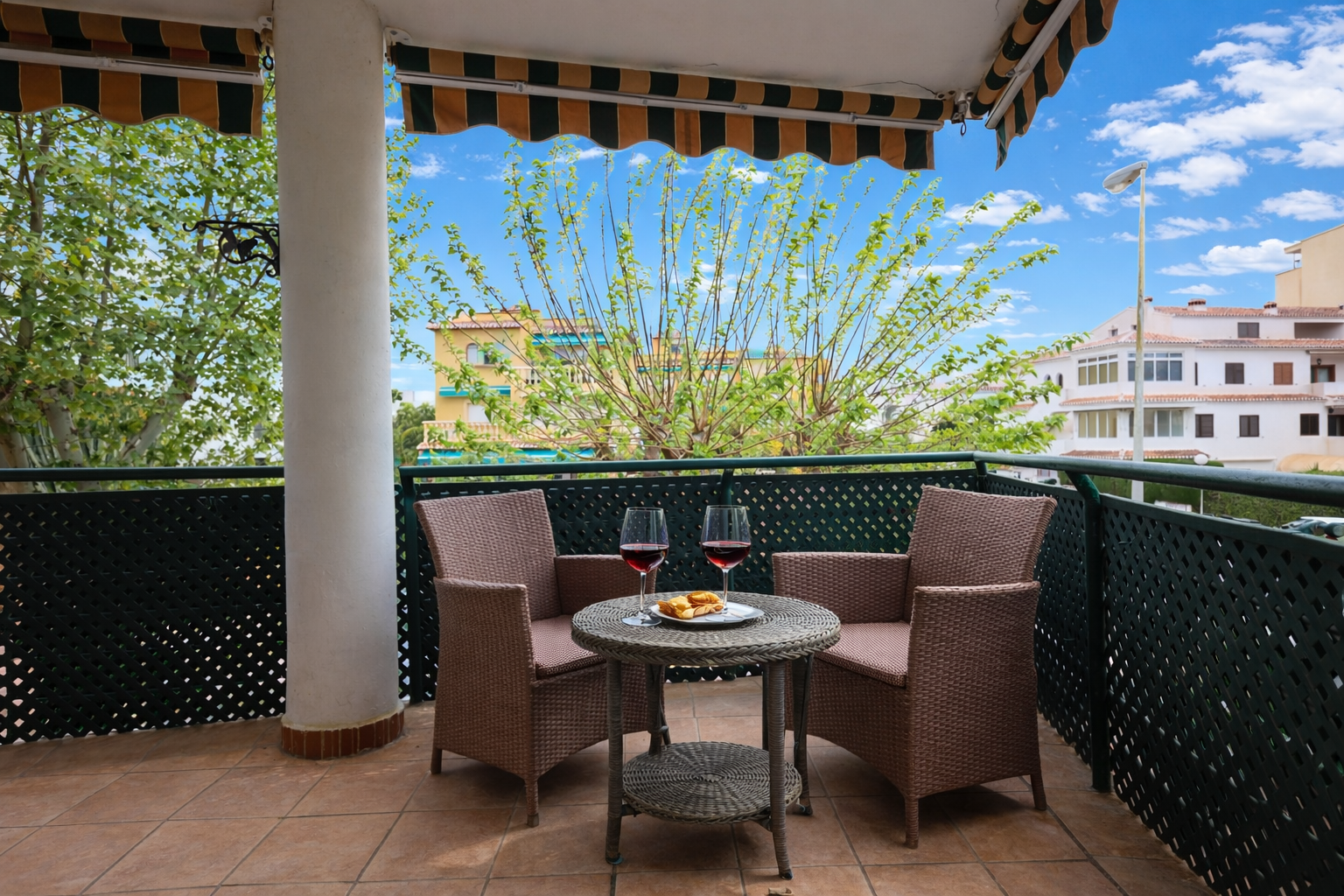 Terraza con suelo de baldosas, toldo a rayas y muebles de mimbre con vistas al exterior.