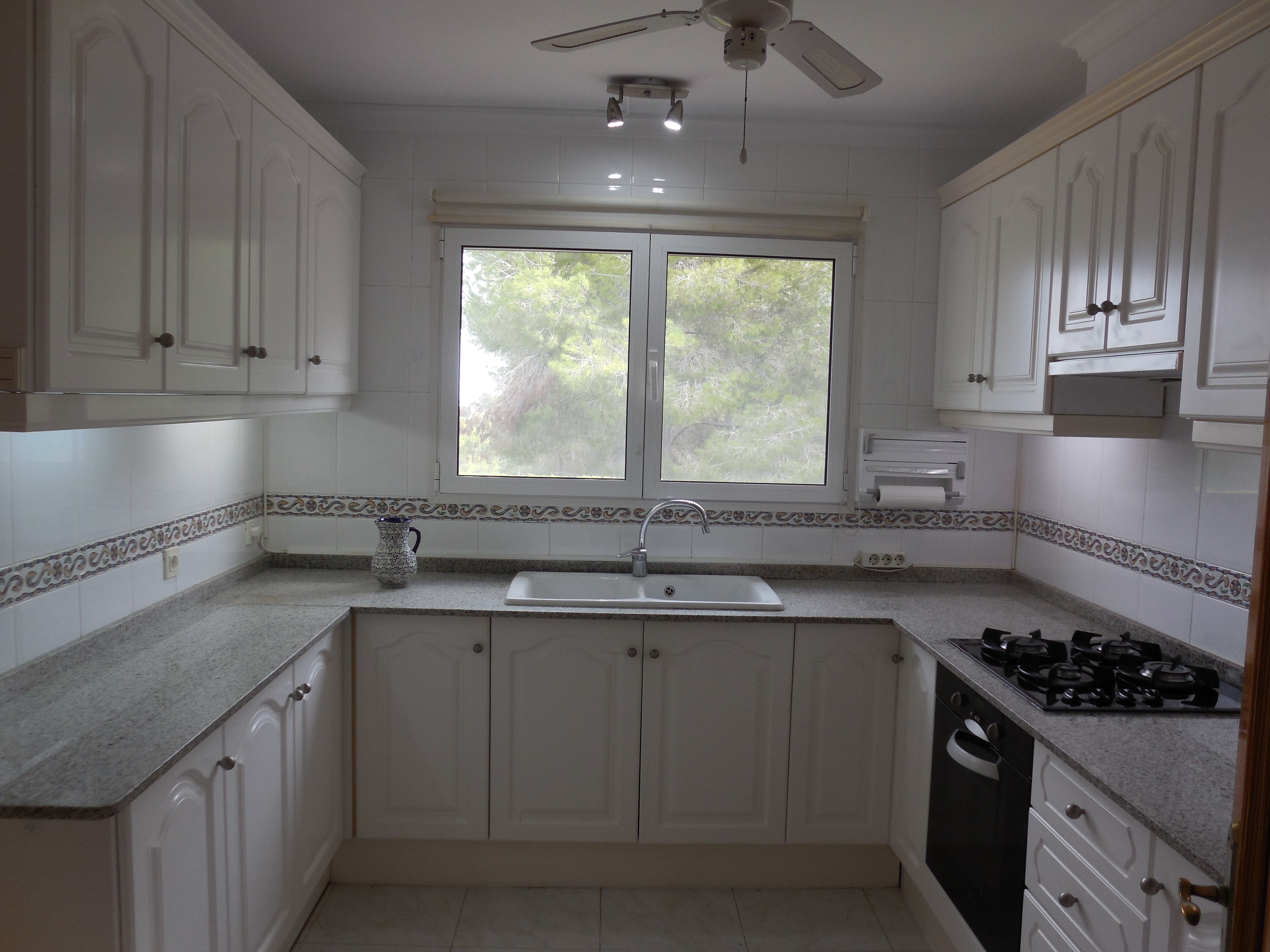 Cocina con encimera de granito gris, armarios blancos clásicos y ventana con vista al exterior.