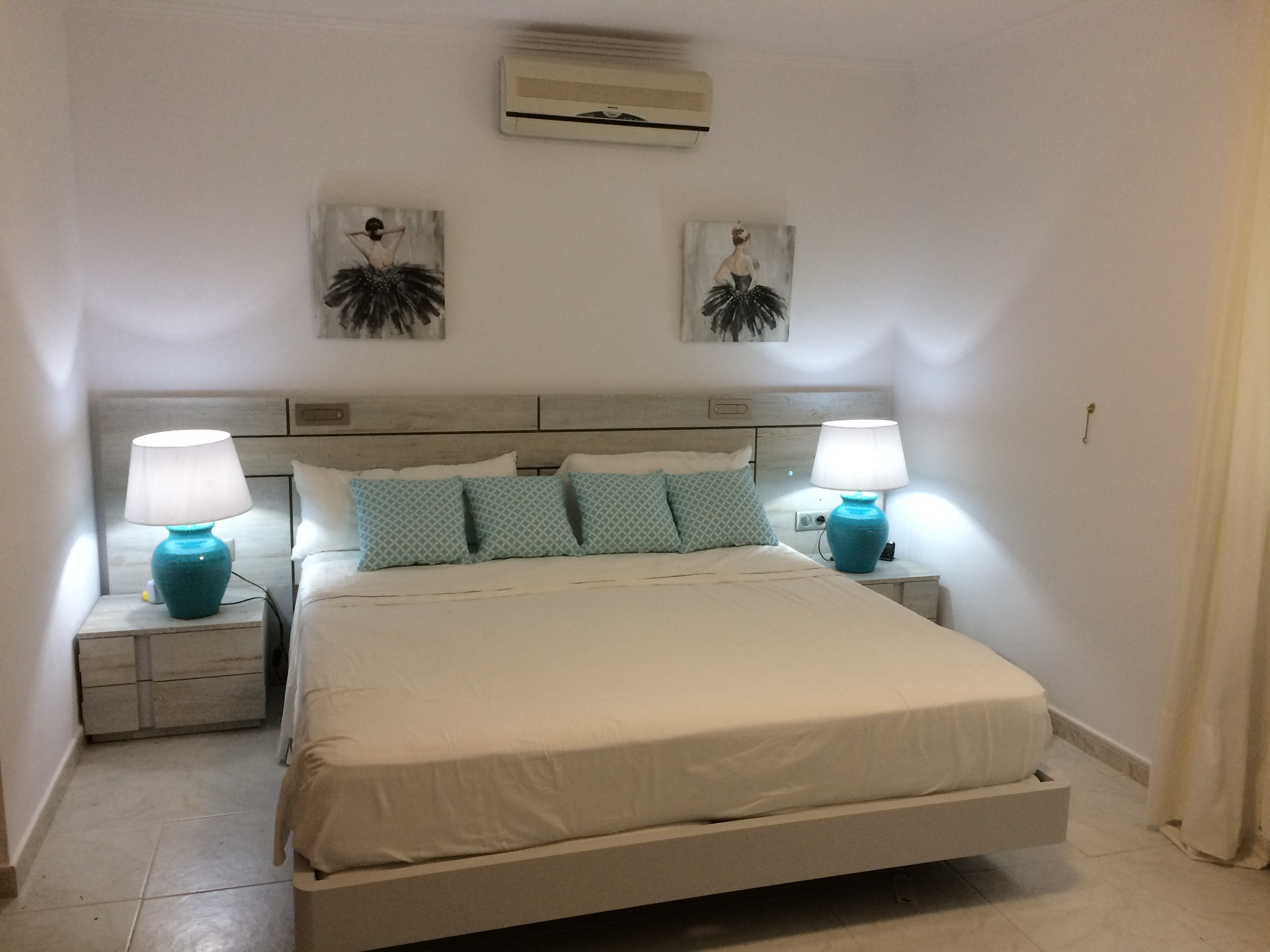 Dormitorio con cama doble, cabecero de madera clara y mesitas de noche a juego con lámparas de cerámica azul.