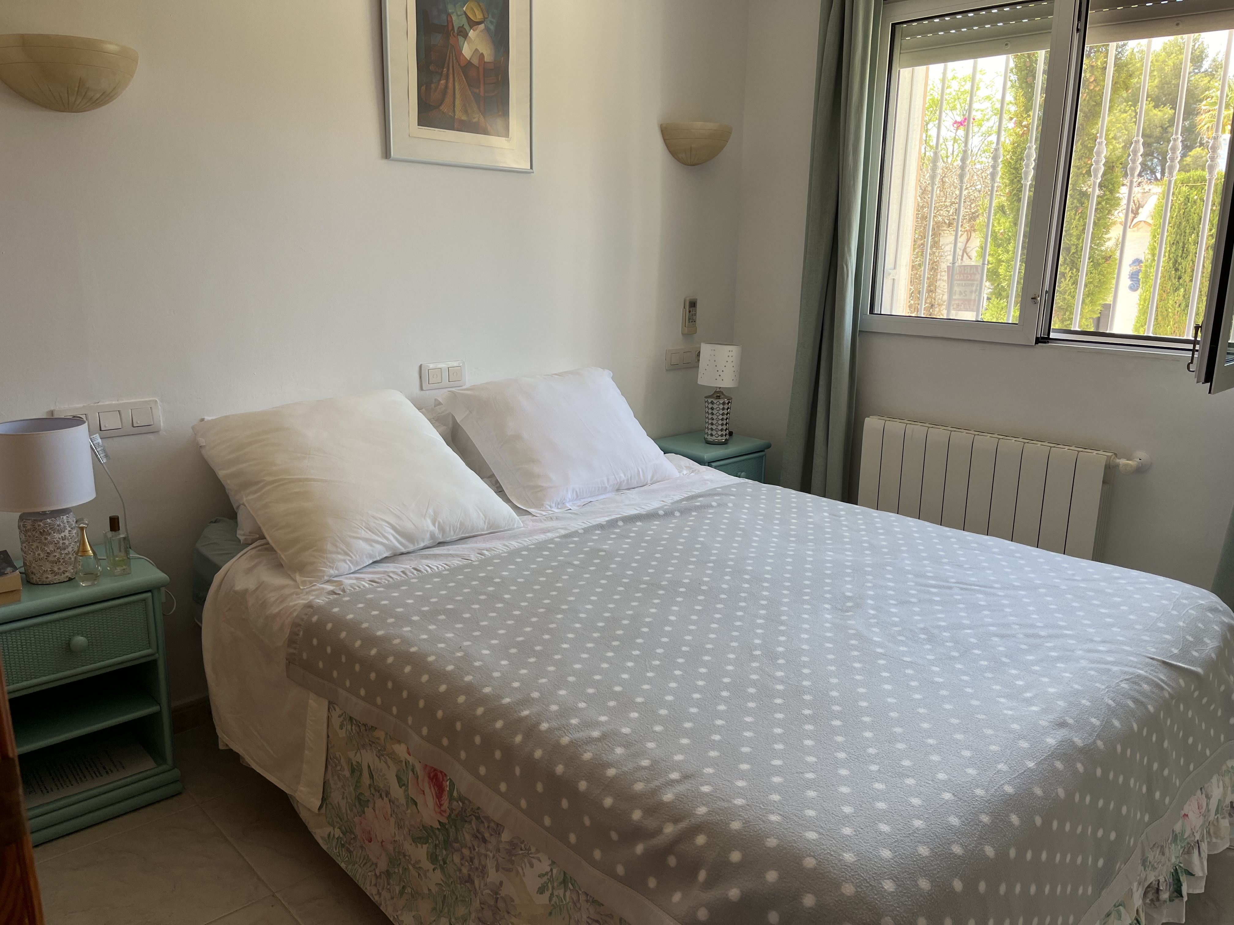 Dormitorio luminoso con cama doble, mesita de noche turquesa y detalles decorativos.