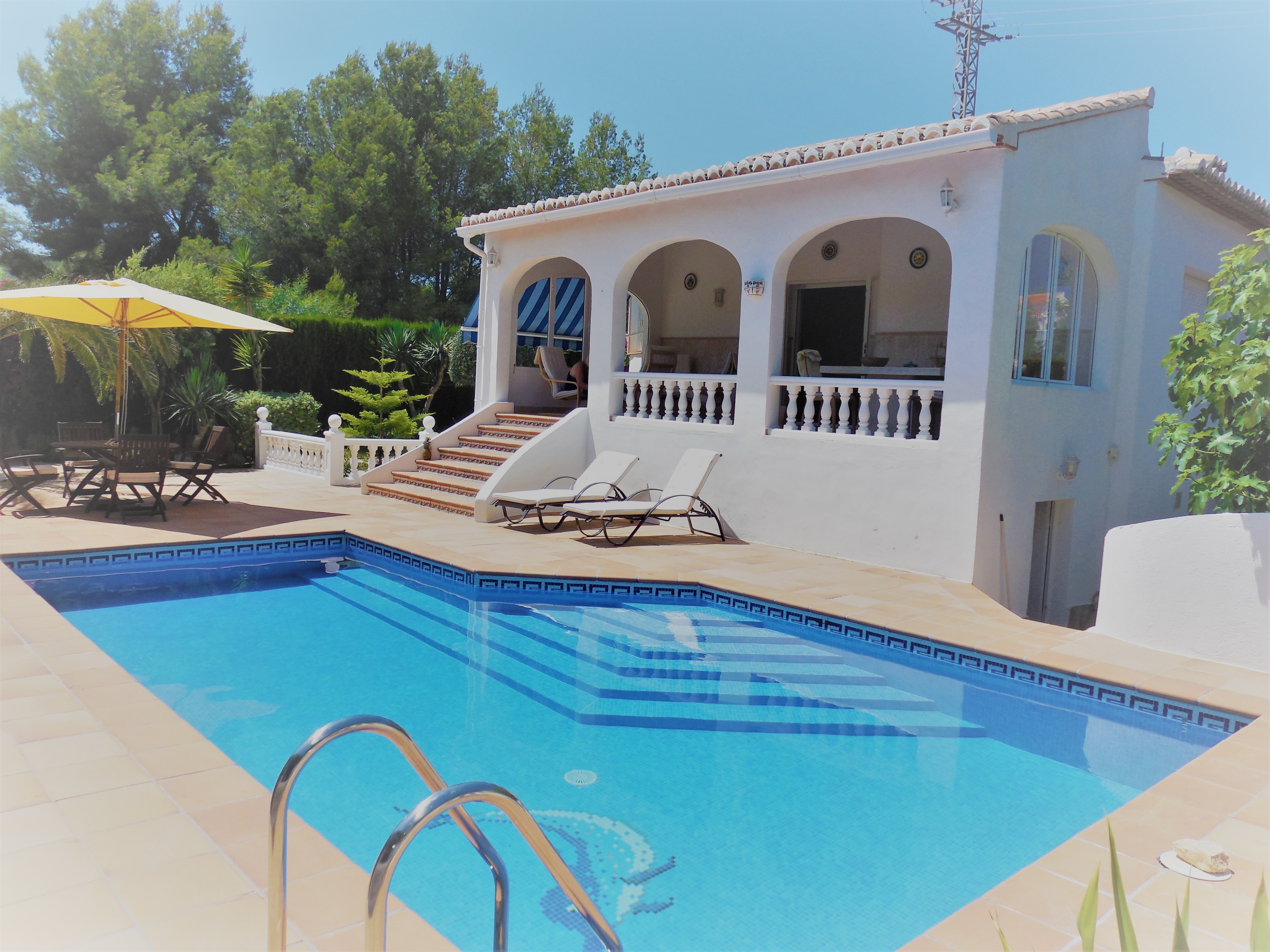 Vista de la piscina con escalones azules y acceso a la terraza cubierta con arcos.