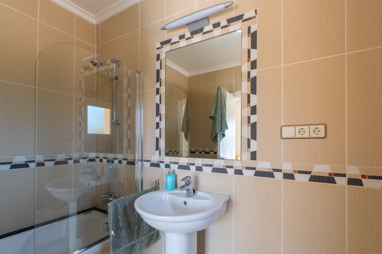 Detalle del baño con lavabo de pedestal y espejo decorativo con mosaicos.