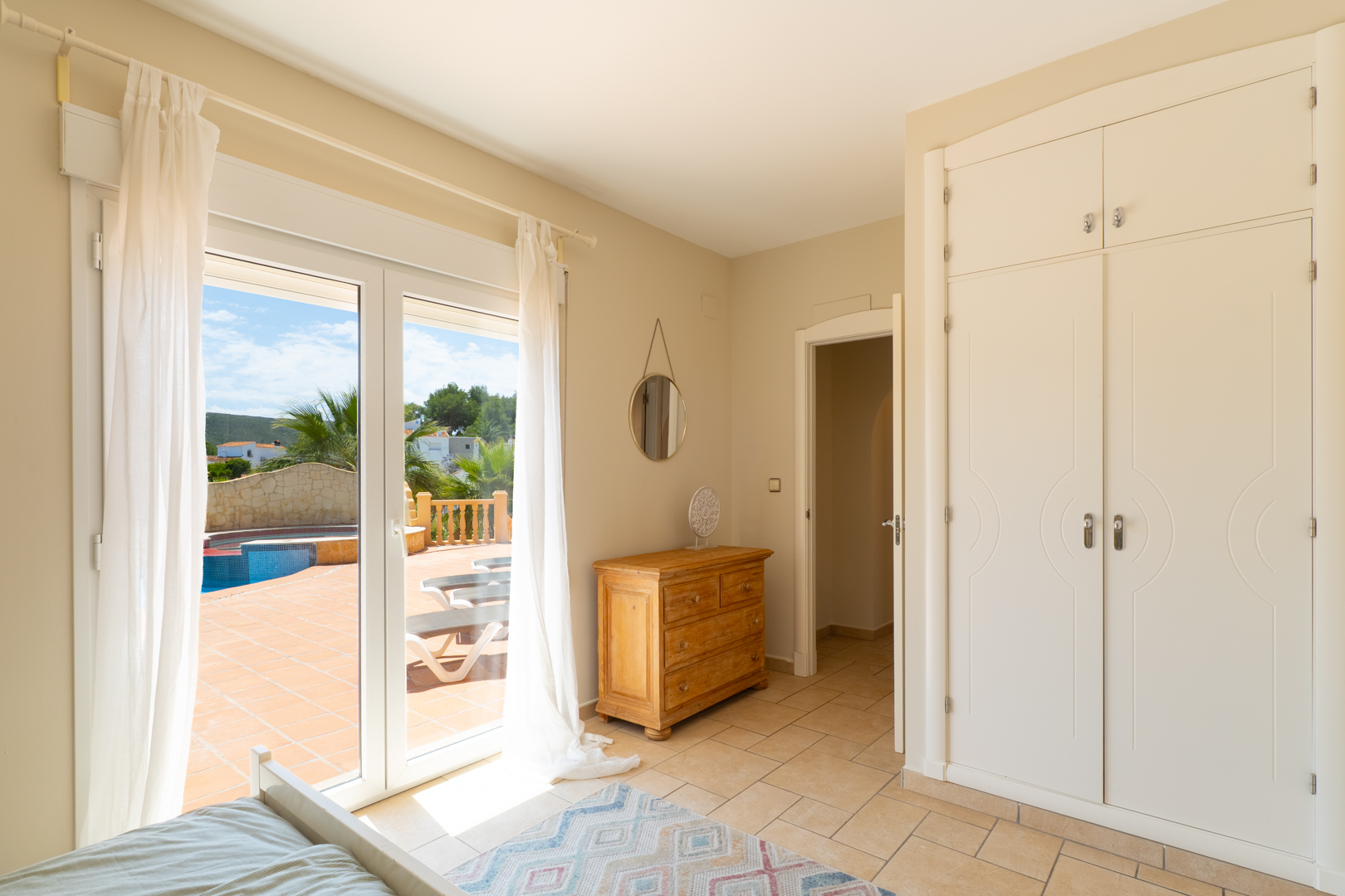 Dormitorio luminoso con acceso a la terraza y piscina. Armario empotrado y cómoda de madera.