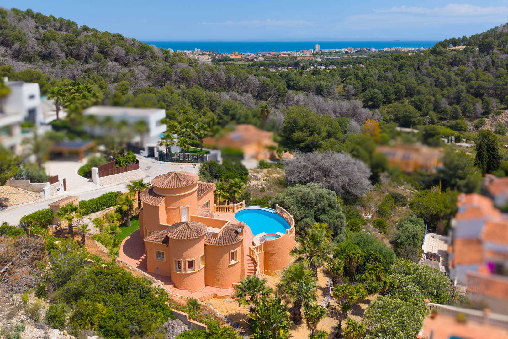 Vista aérea de la villa con piscina azul, rodeada de vegetación y con vistas al mar.