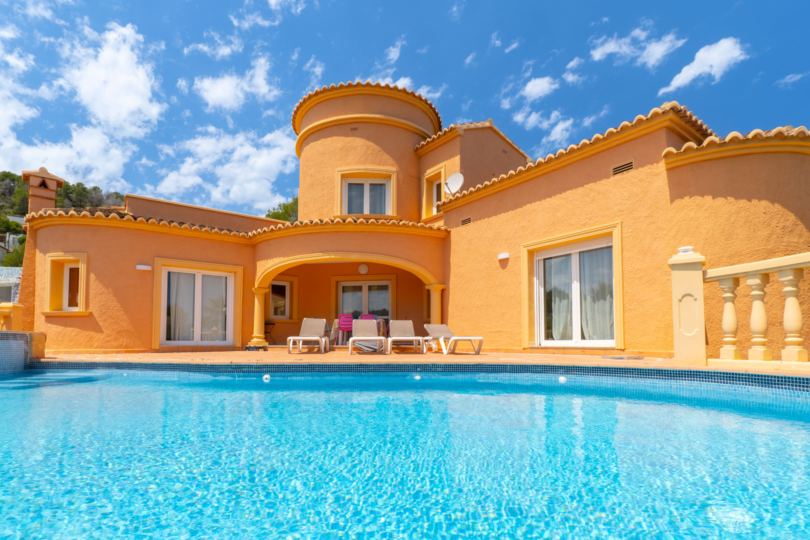 Vista de la fachada principal con piscina turquesa y terraza con tumbonas.