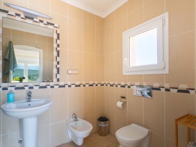 Detalle de baño con azulejos color crema y cenefa decorativa. Incluye lavabo con pedestal, bidé e inodoro.