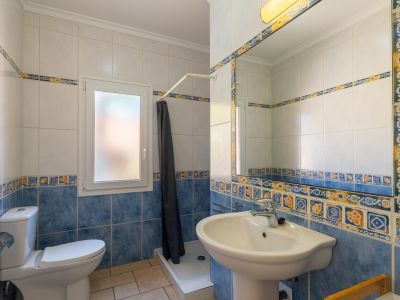 Detalle del baño con azulejos decorativos azules y blancos, lavabo de pedestal y ventana.