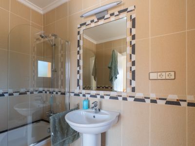 Detalle del baño con lavabo de pedestal y espejo decorativo con mosaicos.