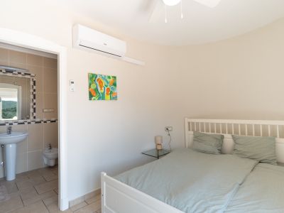Dormitorio luminoso con baño en-suite, decorado con una pintura colorida y cama de madera blanca.