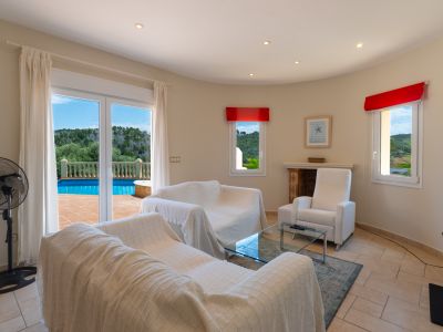 Luminoso salón con acceso a la terraza y piscina. Sofás blancos cubiertos y detalles en rojo.