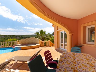 Terraza cubierta con vistas a la piscina y jacuzzi. Mobiliario de exterior y diseño arquitectónico mediterráneo.
